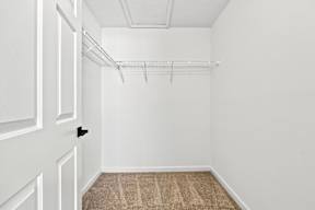A white door with a black handle is on the left side of a room with a carpeted floor and a metal shelf above it.