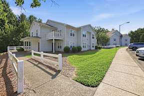 A white picket fence separates a driveway from a grassy area.
