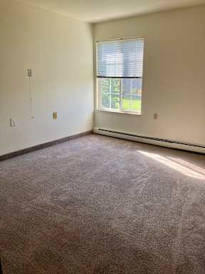 A bedroom with a carpeted floor and a window.