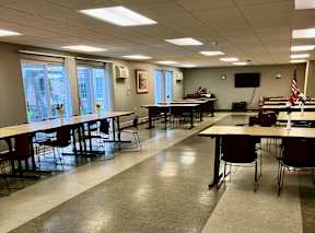 A conference room with tables and chairs and a television on the wall.