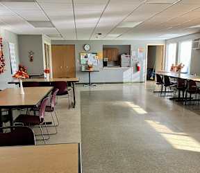 A room with tables and chairs and a kitchen area next to it.