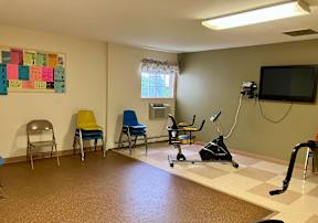 An exercise room with exercise equipment, stacks of chairs, and a television.