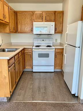 A kitchen with wooden cabinets and white appliances, including a microwave, stove and refrigerator.