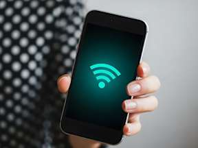 A person is holding a smartphone with a Wi-Fi symbol on the screen.
