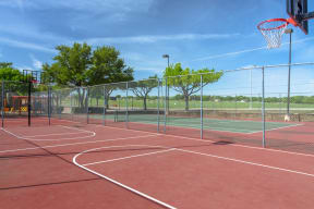 Sports court with basketball hoops and tennis court in the back at Chisholm Place Apartments in Plano, TX