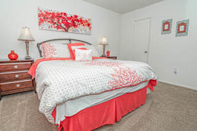 View of bed in model apartment bedroom with red painting on the wall at Laurel Parc apartments in Shreveport, LA.