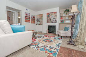 Large model living room with a white couch and a colorful rug facing a fireplace at Laurel Parc apartments in Shreveport, LA.