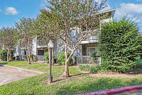 A tree in front of a white building with a balcony at Laurel Parc apartments in Shreveport, LA.