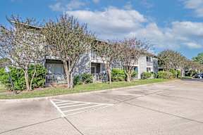 Surface parking lot in front of apartment buildings with a clear blue sky at Laurel Parc apartments in Shreveport, LA.