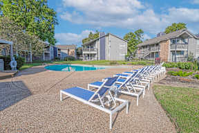 A sunny day at the pool with lounge chairs and apartments in the background at Laurel Parc apartments in Shreveport, LA.