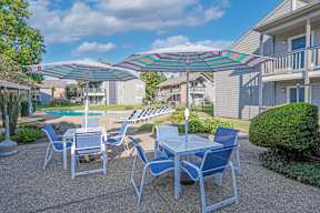 Poolside seating with a table and chairs under a striped umbrella at Laurel Parc apartments in Shreveport, LA.