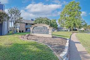 The entrance sign to Laurel Park Apartments is surrounded by a well-maintained lawn and trees at Laurel Parc apartments in Shreveport, LA.