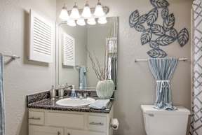 A bathroom with a sink, mirror, and toilet in the model apartment at Stone Canyon apartments in Shreveport, LA.