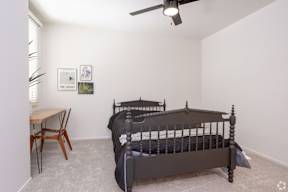 A bedroom with a bed, a table and chairs, and a ceiling fan.