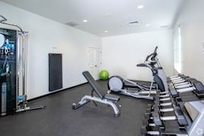 A gym with a variety of equipment including a leg press machine, a rowing machine, and a bench with a green ball on it.