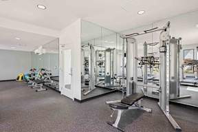 A gym with a variety of equipment including a smith machine, weight bench with free weights, and treadmills.
