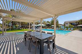 A table and chairs are set up under a white canopy by a pool.