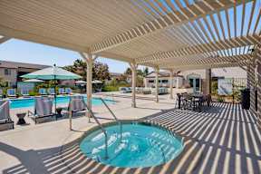 A pool area with a sun shade and a hot tub.