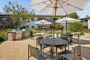 Outdoor BBQ area with grills and tables and chairs under umbrellas.