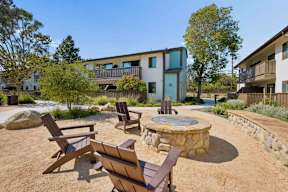 A modern building with a blue door is surrounded by a well-kept garden with a fire pit and chairs.