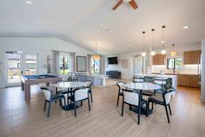 A spacious clubhouse with a billiards table, dining tables, and kitchen.