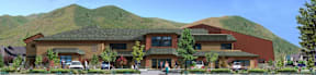 A large building with a green roof and a parking lot in front.