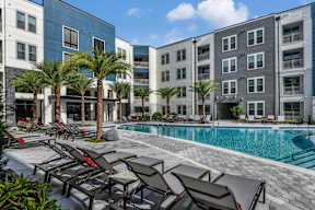 A pool surrounded by lounge chairs and palm trees. at CODA Apartments , Orlando, FL, 32826