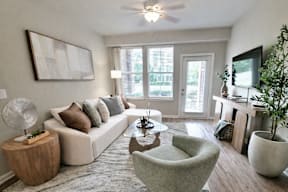 A living room with a white couch, a grey armchair, a wooden side table, and a large painting on the wall. at TRAILSIDE VERDAE Apartments , GREENVILLE, SC, 29607
