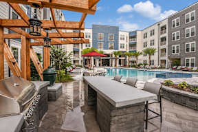 A pool area with a bar and chairs is surrounded by apartment buildings. at CODA Apartments , Florida