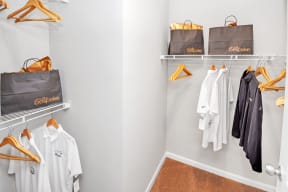 a walk in closet with white clothes and gray bags