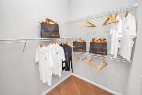 a walk in closet with white clothes and a black tote bag