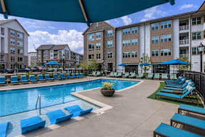 A large swimming pool surrounded by blue lounge chairs and umbrellas at Berewick Pointe Apartments , Charlotte, North Carolina