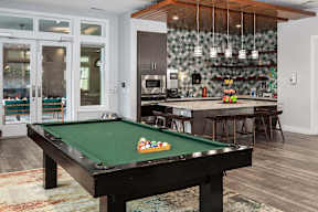 a pool table in a living room with a bar and a kitchen