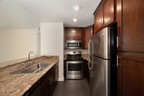 a kitchen with dark wood cabinets and granite countertops and stainless steel appliances at Croft Plaza Apartments, West Hollywood, CA