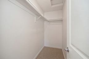 A large extended bedroom closet with a white door and white walls