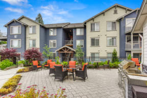 Community outdoor lounge area with chairs and cushions and the BBQ area is located in the same area.   