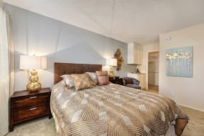 Bedroom with Queen Sized Mattress, Medium Bedside Dresser with Lit Lamp on both sides of Bed, Small Arm Chair, Closet, and Carpeted Flooring