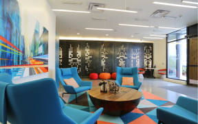 a lobby with blue chairs and a coffee table with a large painting on the wall