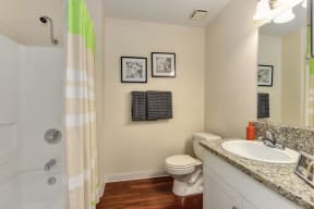 Model home bathroom with shower enclosure with shower curtain, granite countertops, and white cabinets. at Monte Bello Apartments, Sacramento