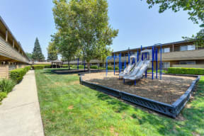 Community Outdoor Playground with Slides, Woodchip Floor and Grass  at Olympus Park Apartments, Roseville, CA, 95661