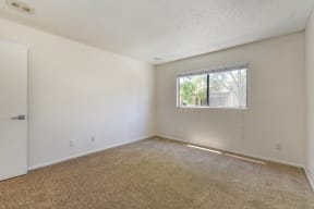 Vacant apartment bedroom with carpeting, white walls and window with blinds.