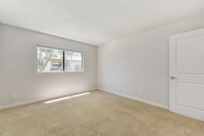 A vacant apartment bedroom with carpet and a window with blinds.