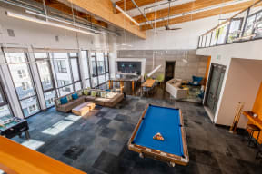 Community Clubhouse with Pool Table, Hardwood Inspired Staircase, Tan Sofa, Blue Sofa and Hanging Ceiling Lights