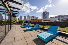 an outdoor deck with blue lounge chairs and a city skyline in the background