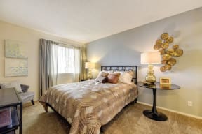Model home bedroom with larger bed, side tables with decorative wall art. There is plush carpeting in the bedroom and a large window 