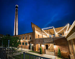 Cotton Mill Apartments exterior, open-walled community patio with stringlights and stairs, and a water tower overlooking it.