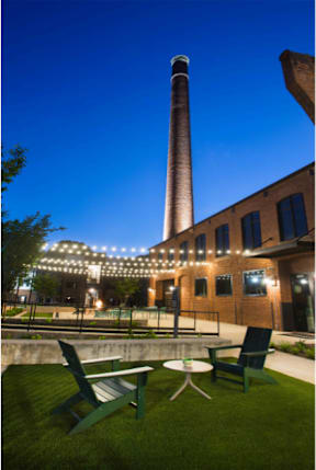 Cotton Mill Apartments outside chairs with chimney at night, lit up by string lights