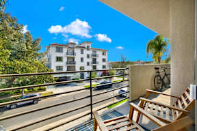 A balcony with a chair and a bicycle is overlooking a street with cars and buildings.