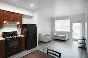 A black refrigerator sits in a kitchen with wooden cabinets and a stove.