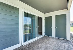 Patio with a sliding glass door at Somerset Lakes Apartments, offering a private outdoor space for relaxation. and a grey door.